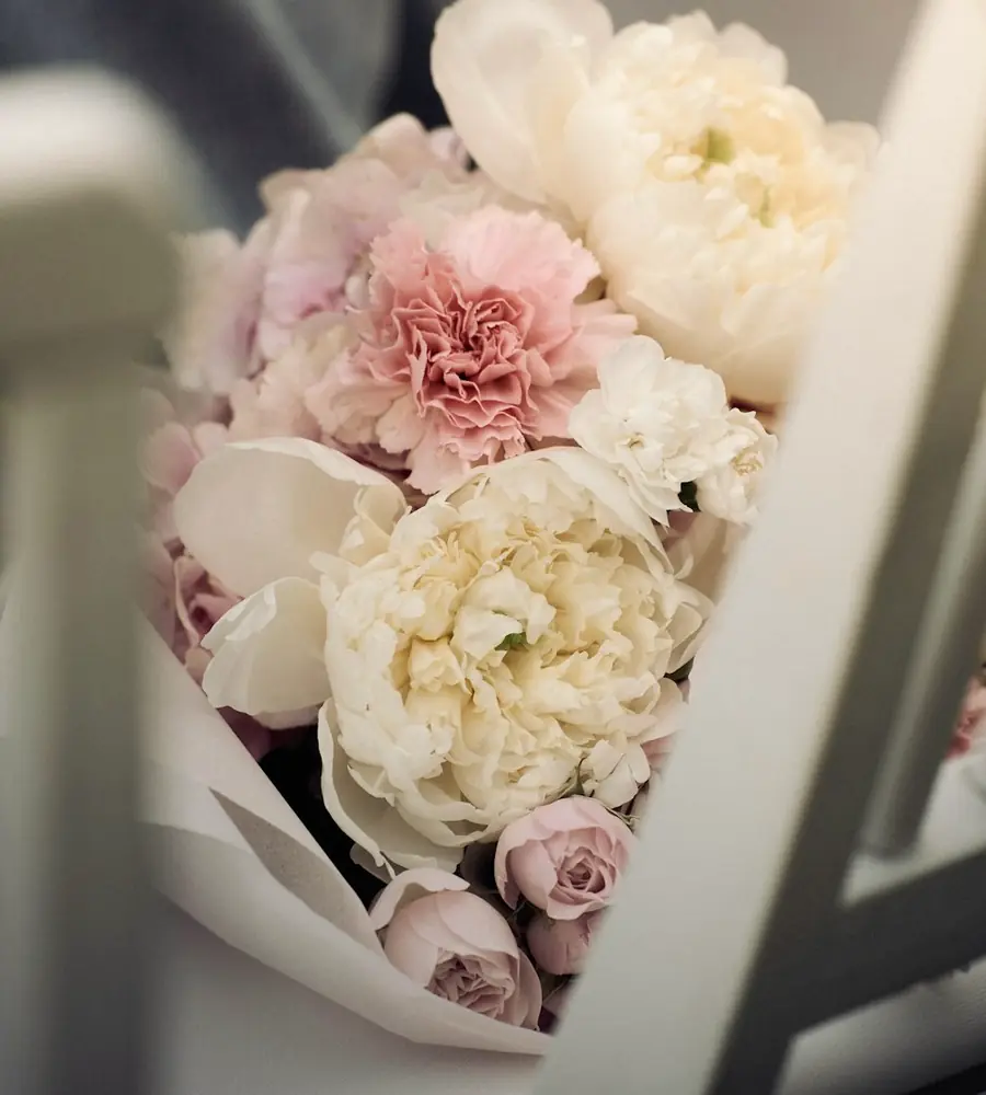 A bouquet of cream and blush peonies wrapped in paper